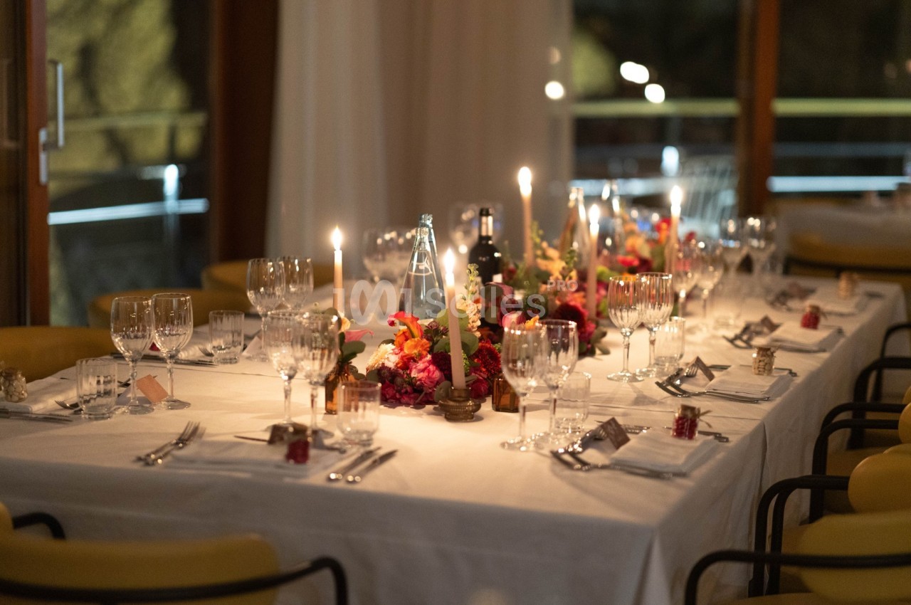 Table élégamment dressée avec bougies, fleurs colorées, verres et couverts dans une ambiance chaleureuse.