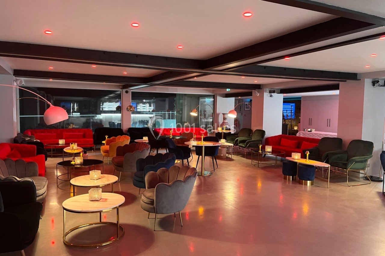Salle moderne avec fauteuils colorés, tables rondes en bois clair et éclairage tamisé rouge.
