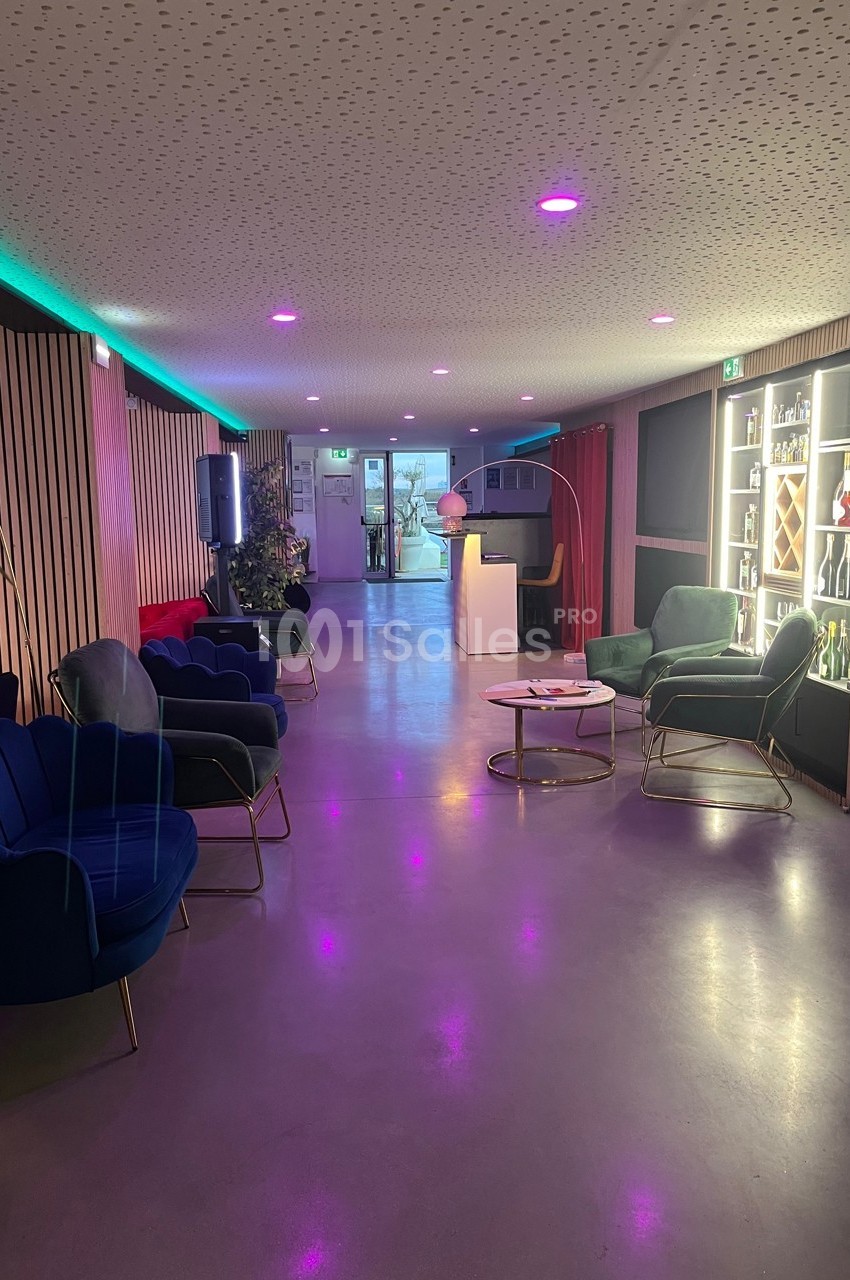 Espace lounge moderne avec fauteuils colorés, éclairage tamisé et étagères illuminées contenant des bouteilles.
