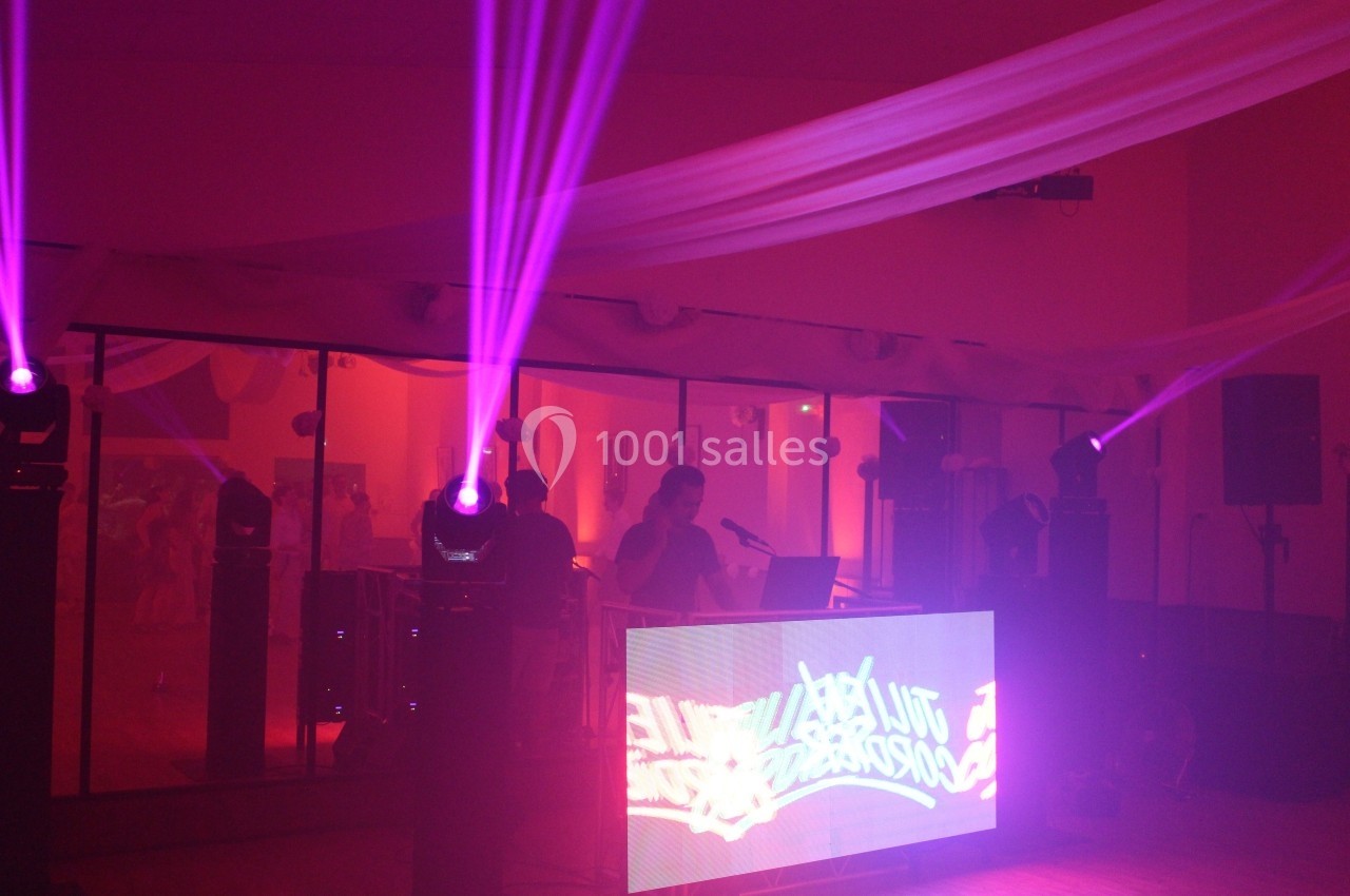 Salle de réception éclairée par des lumières violettes, avec un DJ devant une table lumineuse et des miroirs en arrière-plan.
