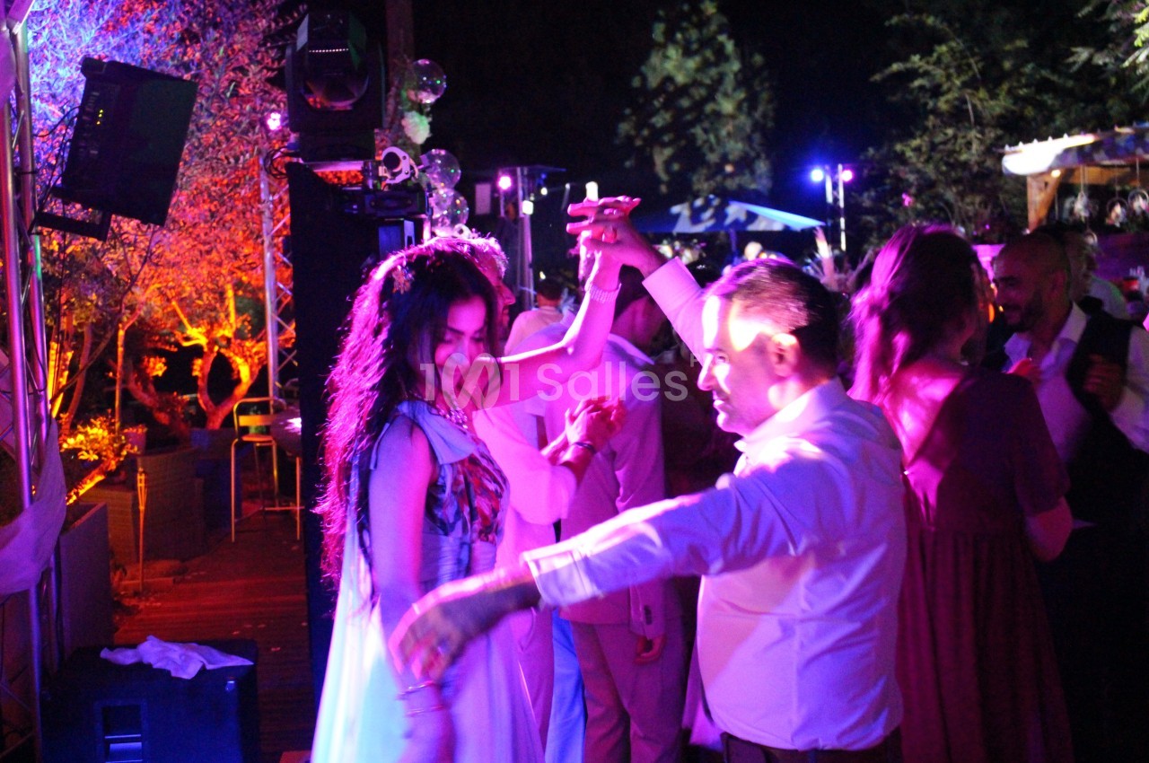 Un homme et une femme dansent sous des lumières colorées lors d'une fête en plein air, entourés d'autres invités.