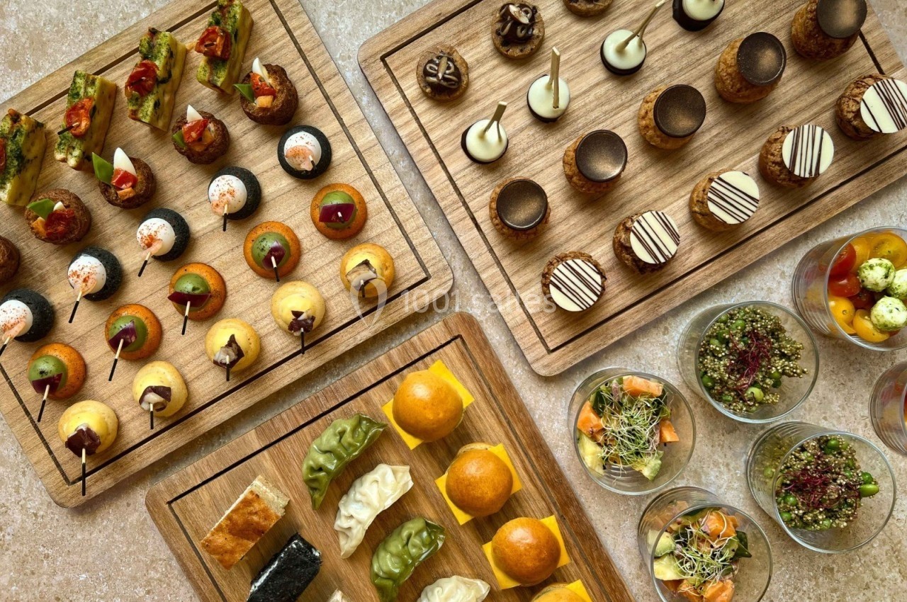 Plateaux en bois garnis de bouchées salées et sucrées, accompagnés de verrines colorées sur une table beige.