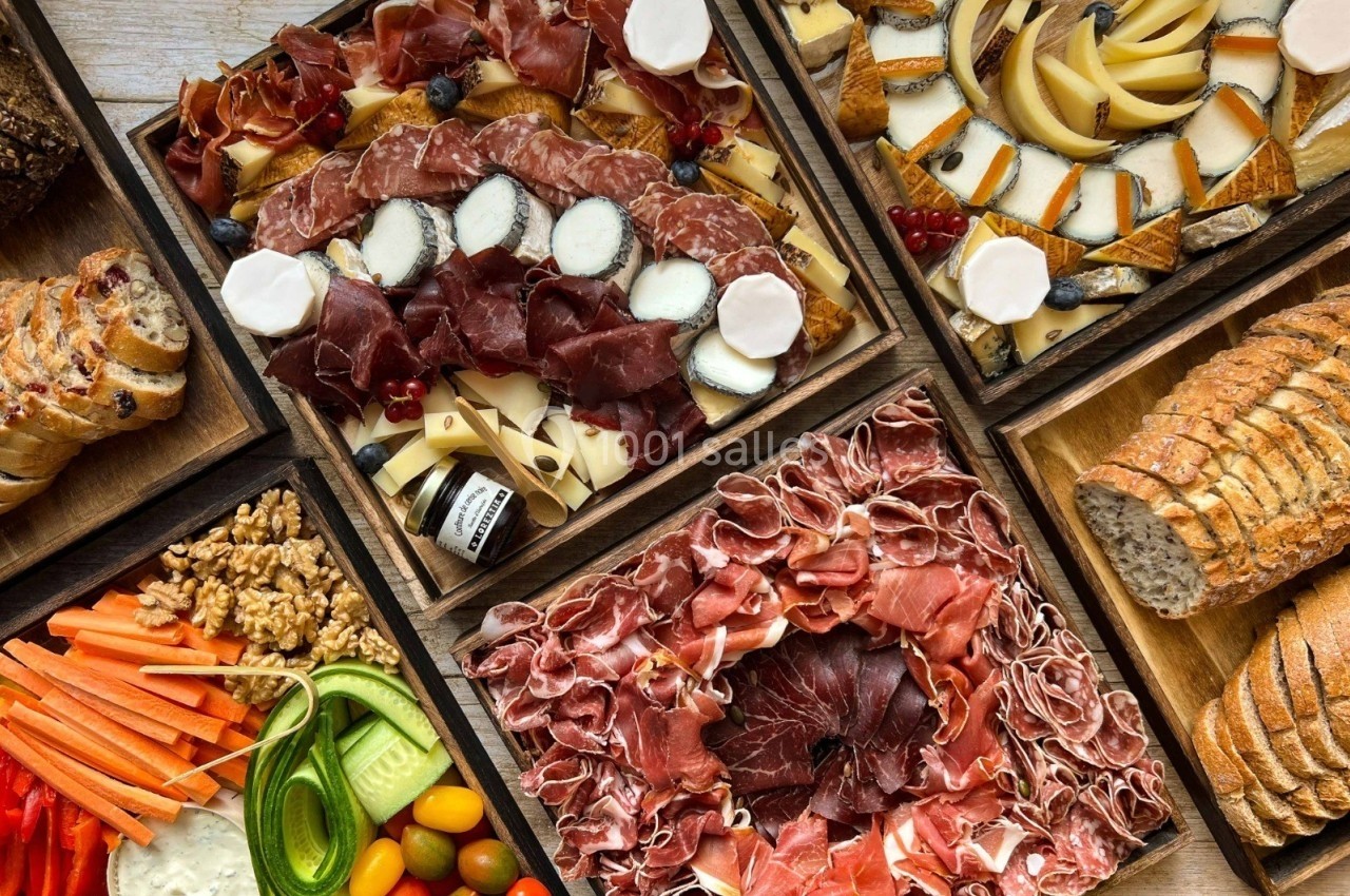 Plateaux variés de charcuterie, fromages, légumes frais, fruits secs et pains disposés sur une table en bois.