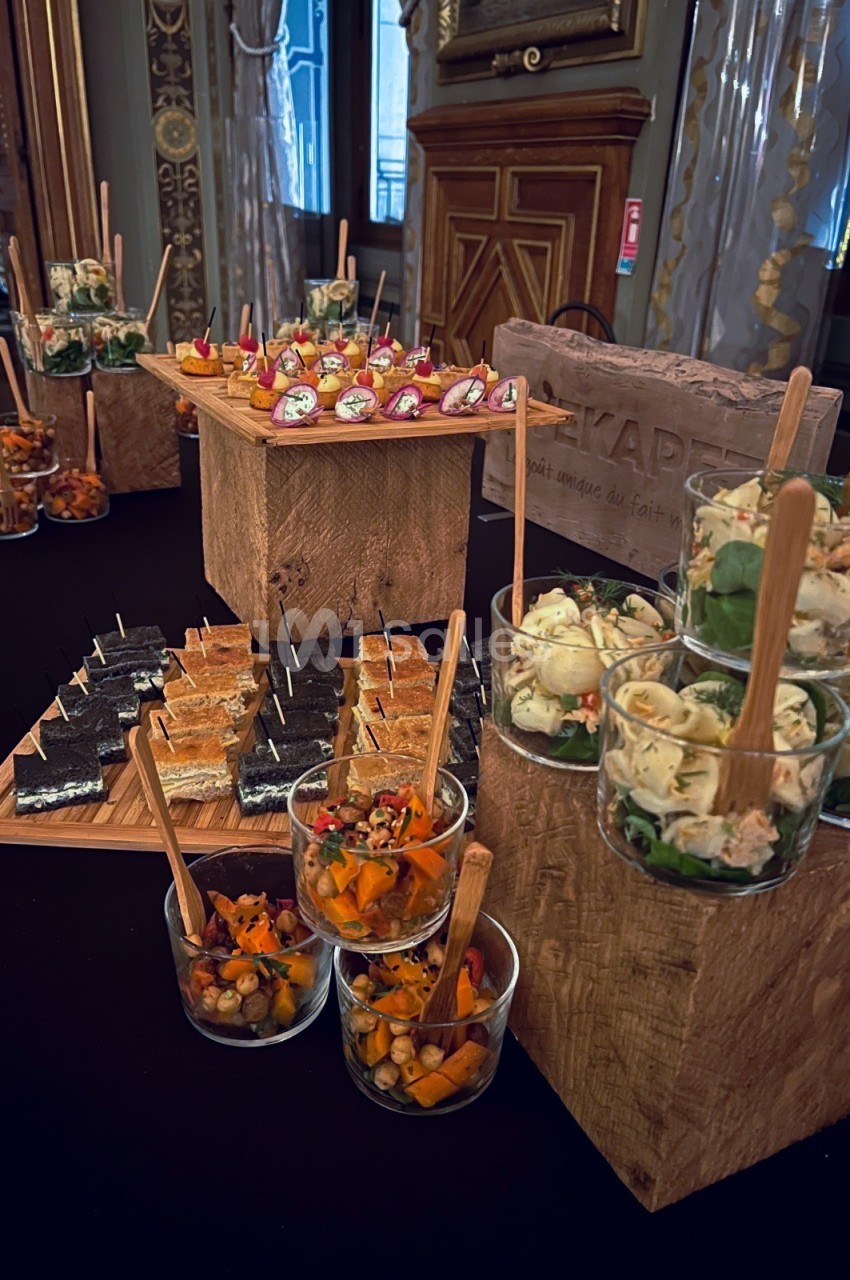 Buffet de verrines et amuse-bouches variés disposés sur des présentoirs en bois dans une salle élégante.