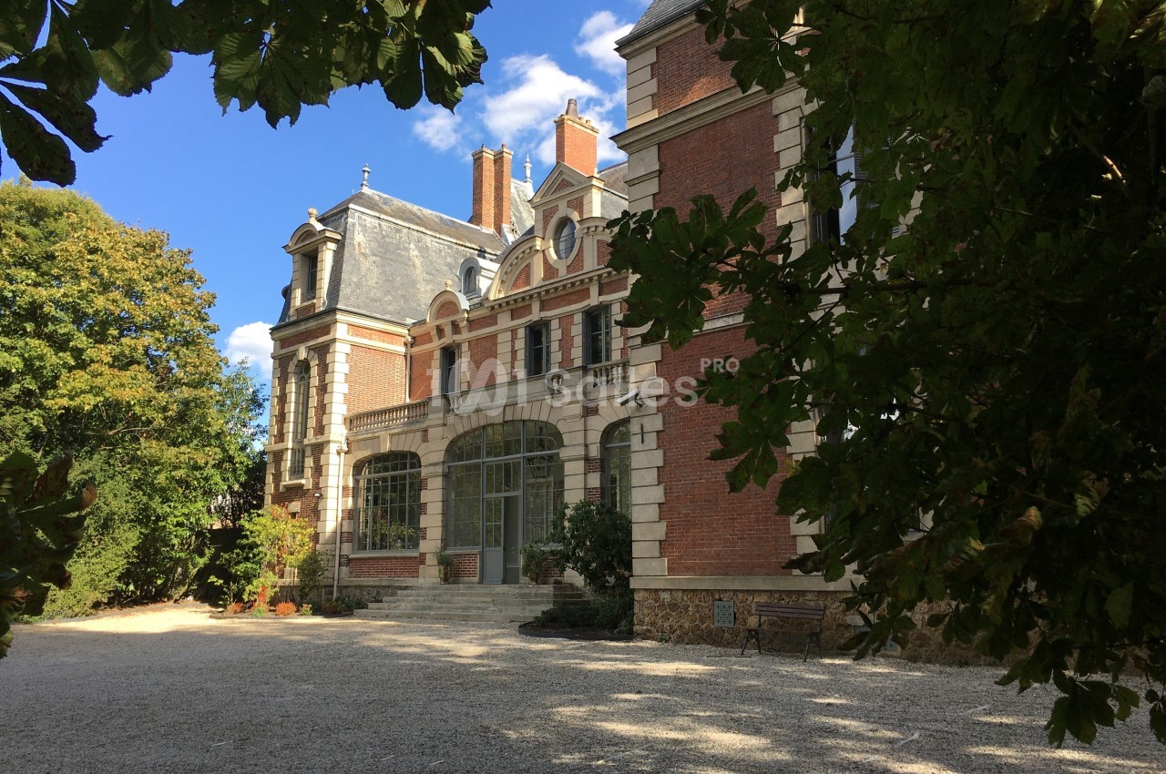Façade d'un manoir en briques rouges entouré de végétation, avec une allée gravillonnée au premier plan.