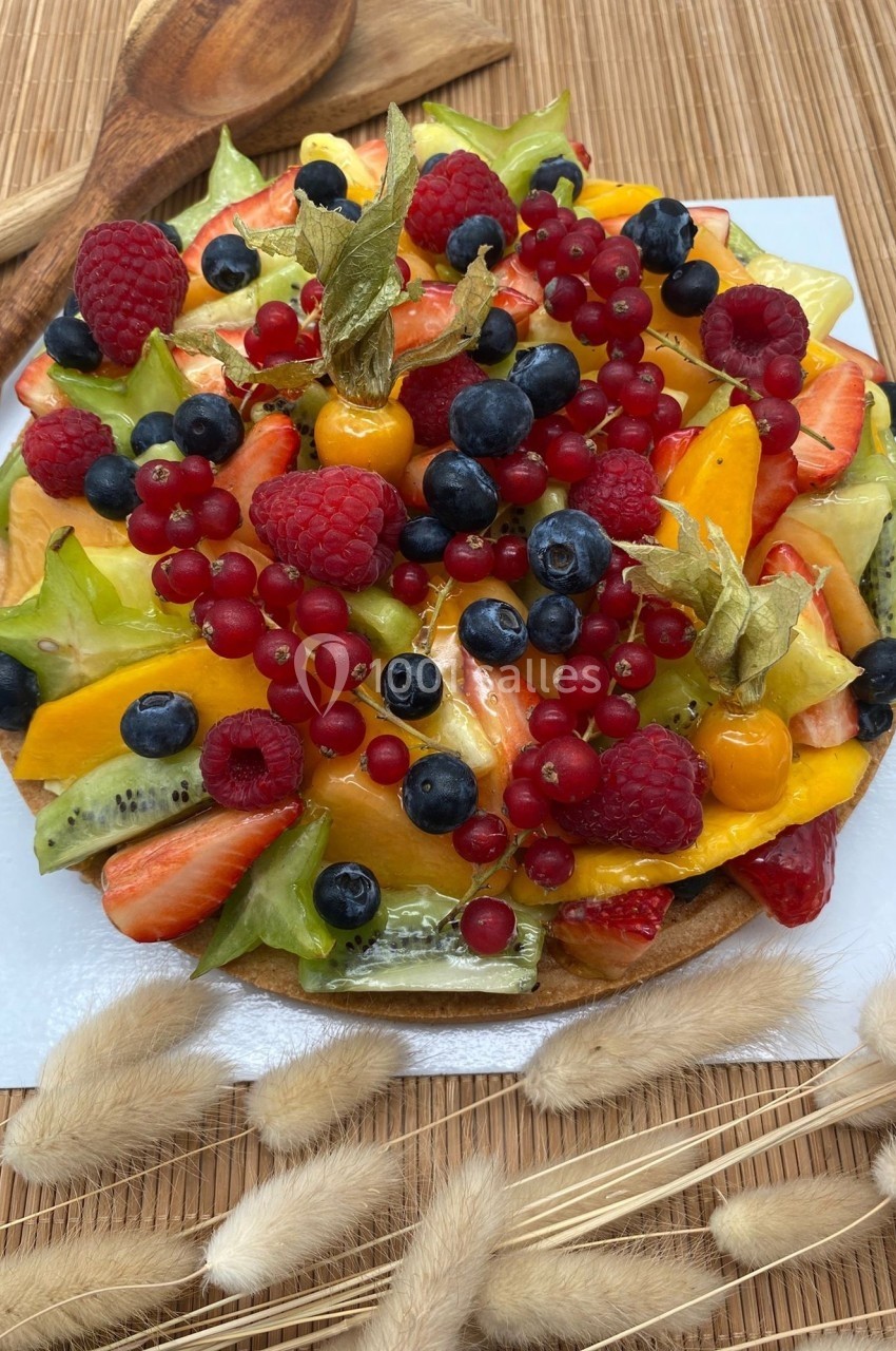 Tarte garnie de fruits frais variés, dont fraises, myrtilles, groseilles, physalis et tranches de carambole.