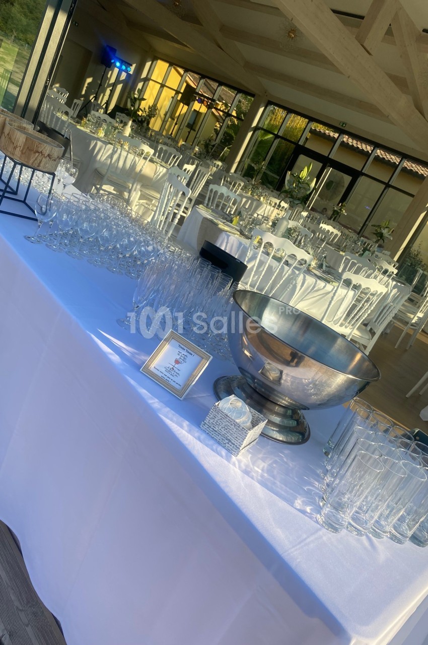 Table dressée avec des verres, un seau à champagne et des décorations, dans une salle lumineuse avec des chaises blanches.