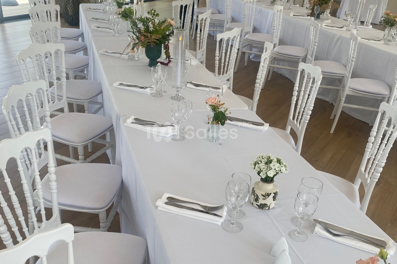 Salle de réception avec tables dressées, nappes blanches, chaises assorties et décorations florales.