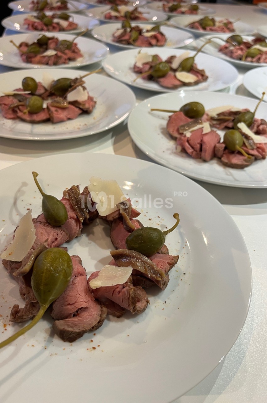 Assiettes de carpaccio de bœuf garnies de câpres, anchois et copeaux de parmesan, disposées sur une table.