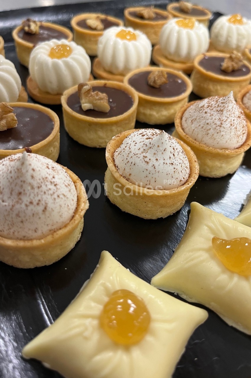 Assortiment de mini-pâtisseries sur un plateau, comprenant tartelettes au chocolat, à la crème et garnies de noix ou de…