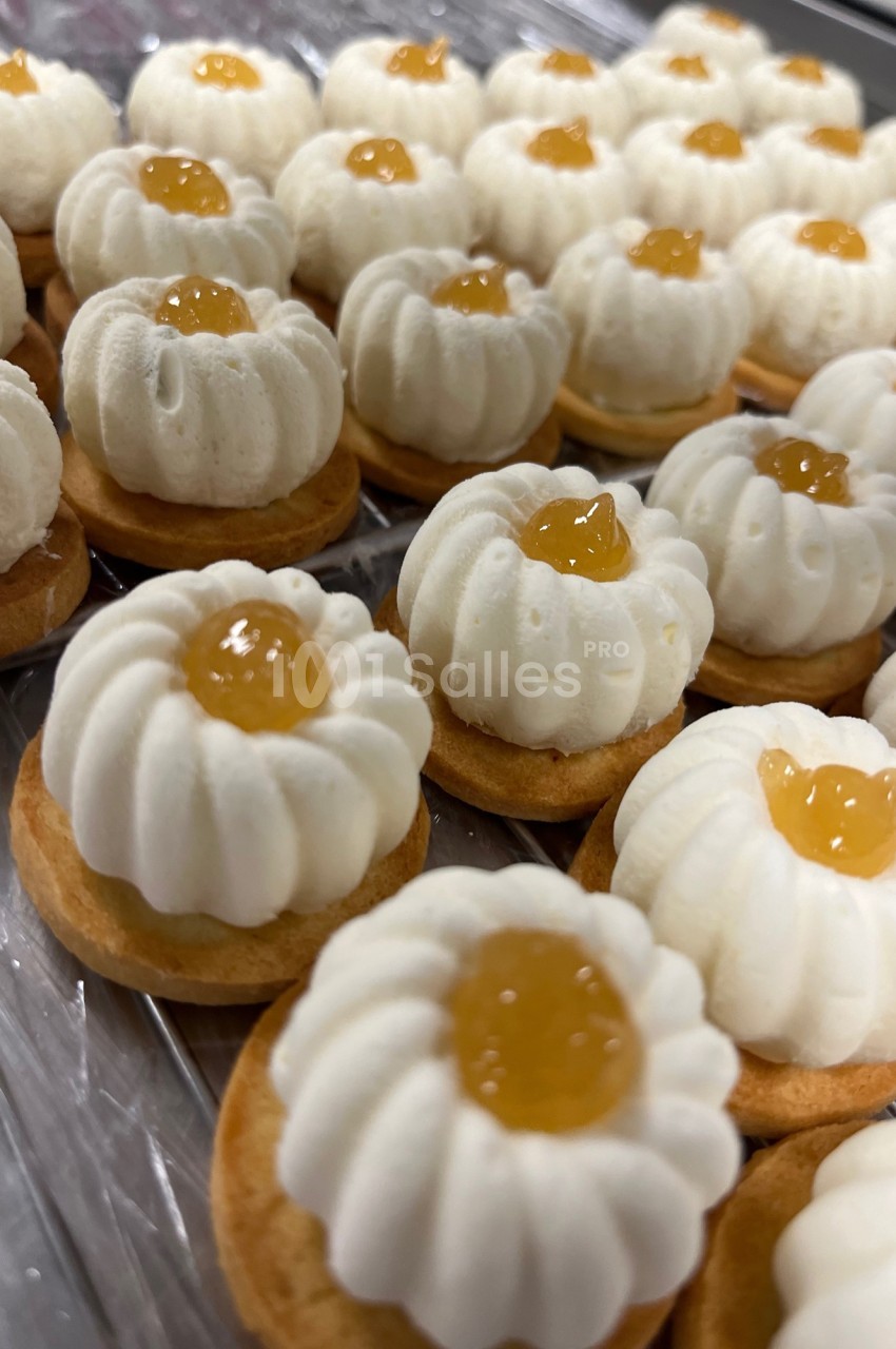Petits biscuits garnis de crème blanche et d'une touche de confiture jaune, alignés sur une surface transparente.