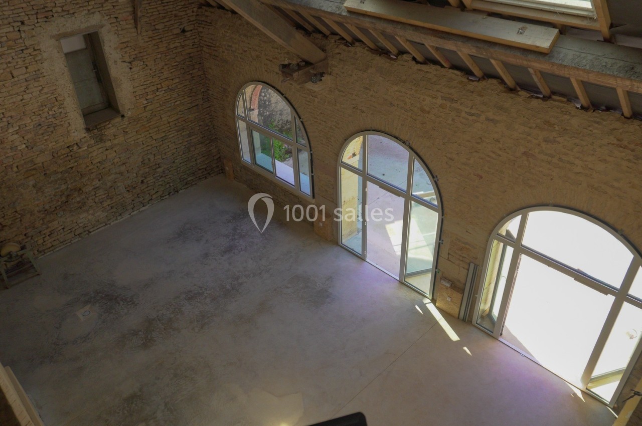 Intérieur d'un bâtiment en pierre avec de grandes arches vitrées laissant entrer la lumière naturelle.