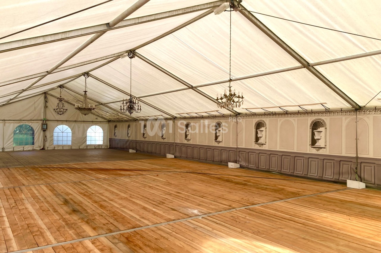 Intérieur d'une grande tente avec plancher en bois, murs décorés de moulures et lustres suspendus.