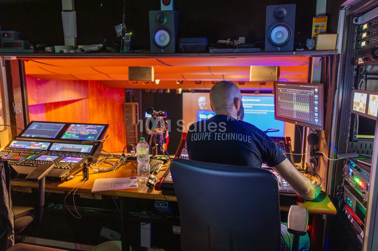 Technicien dans une régie audiovisuelle supervisant des équipements pour un événement en direct sur scène.