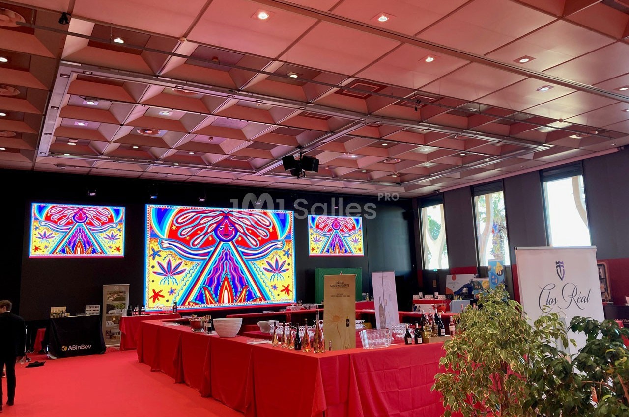 Salle d'exposition avec stands, écrans lumineux affichant des motifs colorés et décoration rouge dominante.