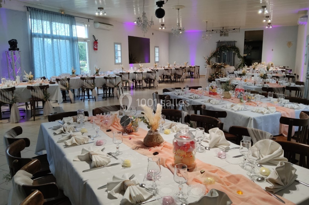 Salle de réception décorée pour un événement, avec tables dressées, nappes blanches et décorations florales.