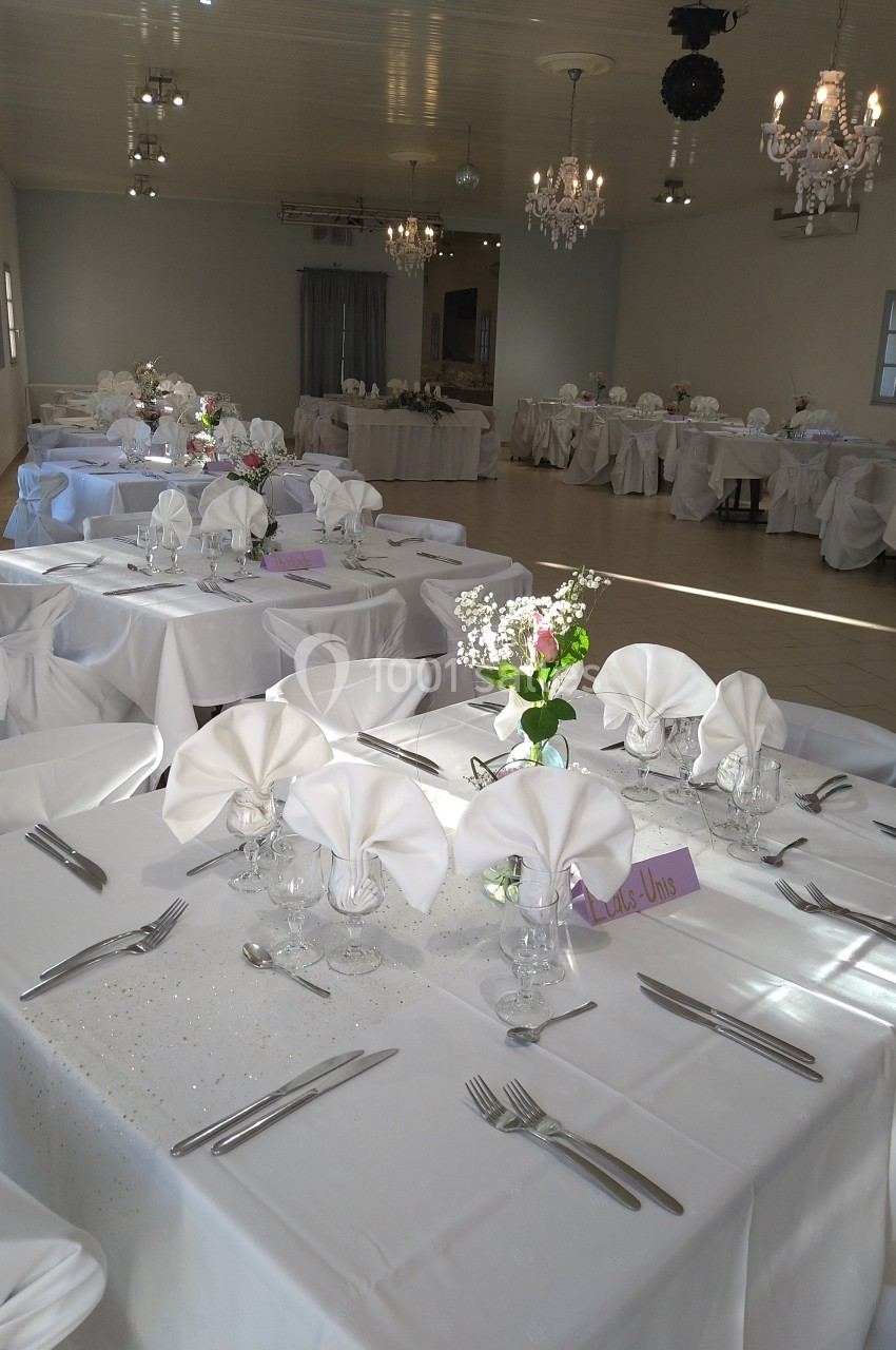 Salle de réception décorée avec des tables dressées, nappes blanches, serviettes pliées et arrangements floraux.
