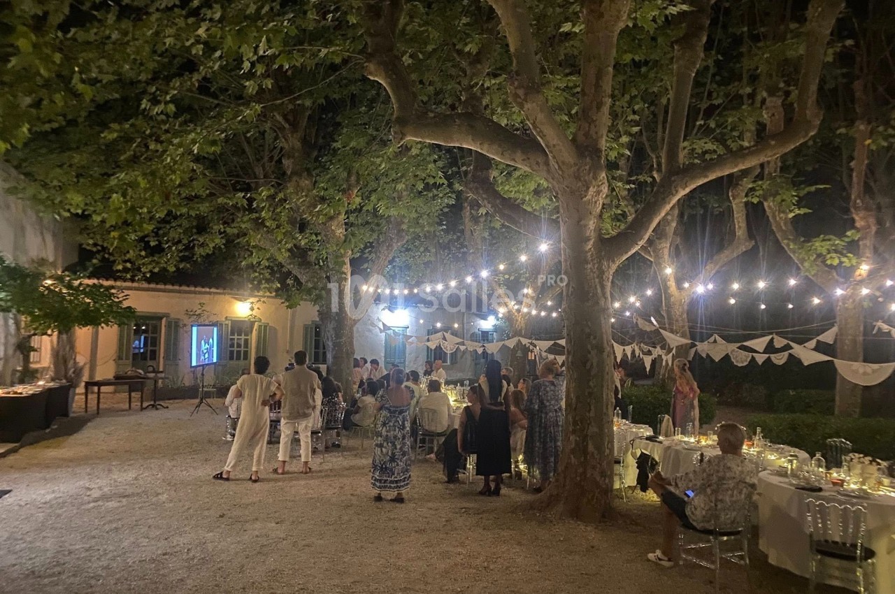Groupe de personnes rassemblées en soirée dans un jardin éclairé par des guirlandes lumineuses, avec tables décorées.
