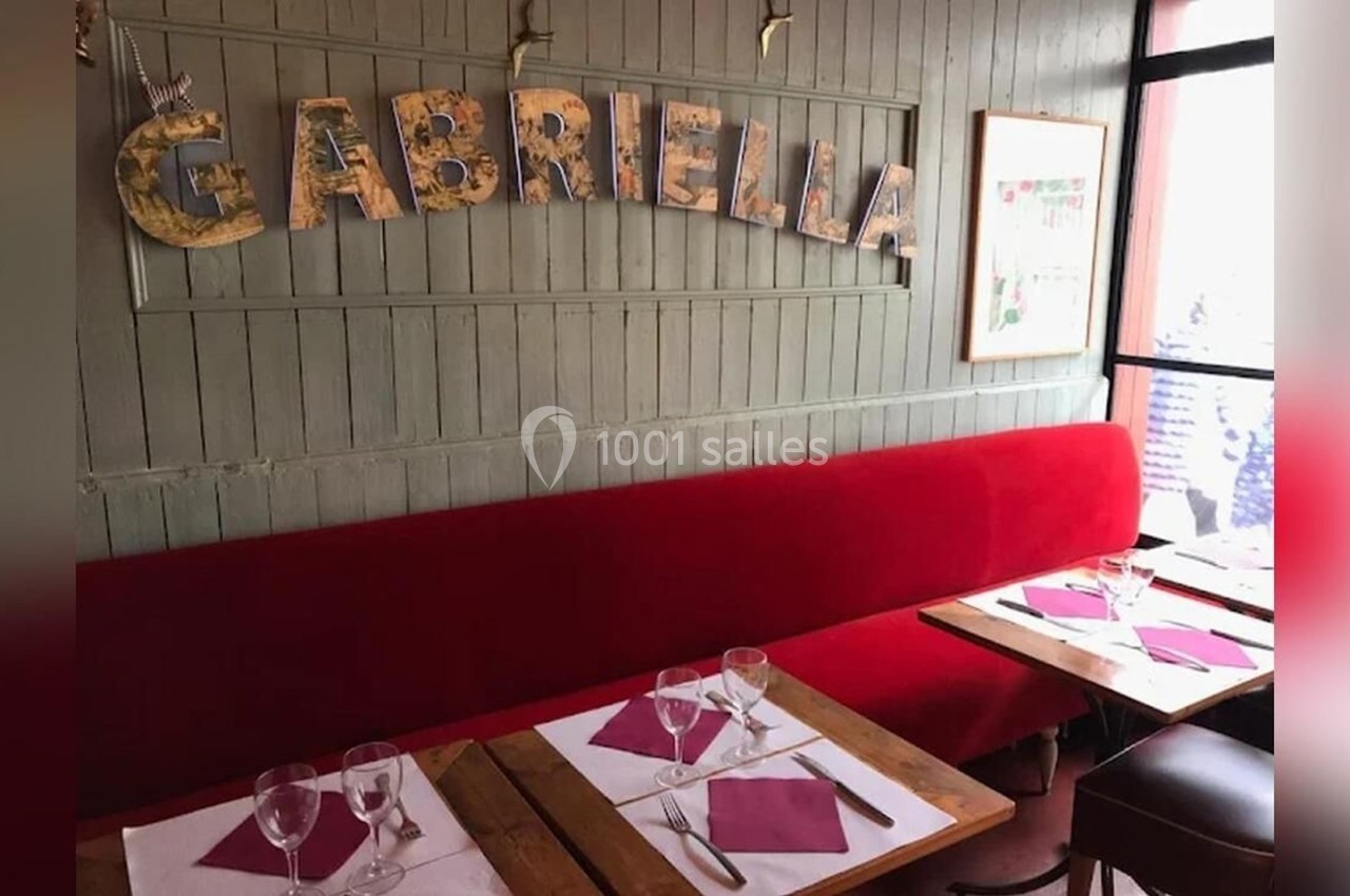 Banquettes rouges et tables dressées dans un restaurant avec le mot ’Gabriella’ affiché sur un mur en bois.