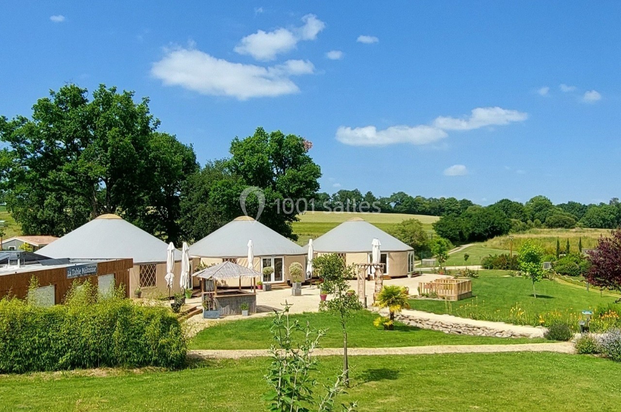 Vue d'un domaine avec plusieurs bâtiments ronds, entouré de verdure et d'un jardin paysager sous un ciel bleu.