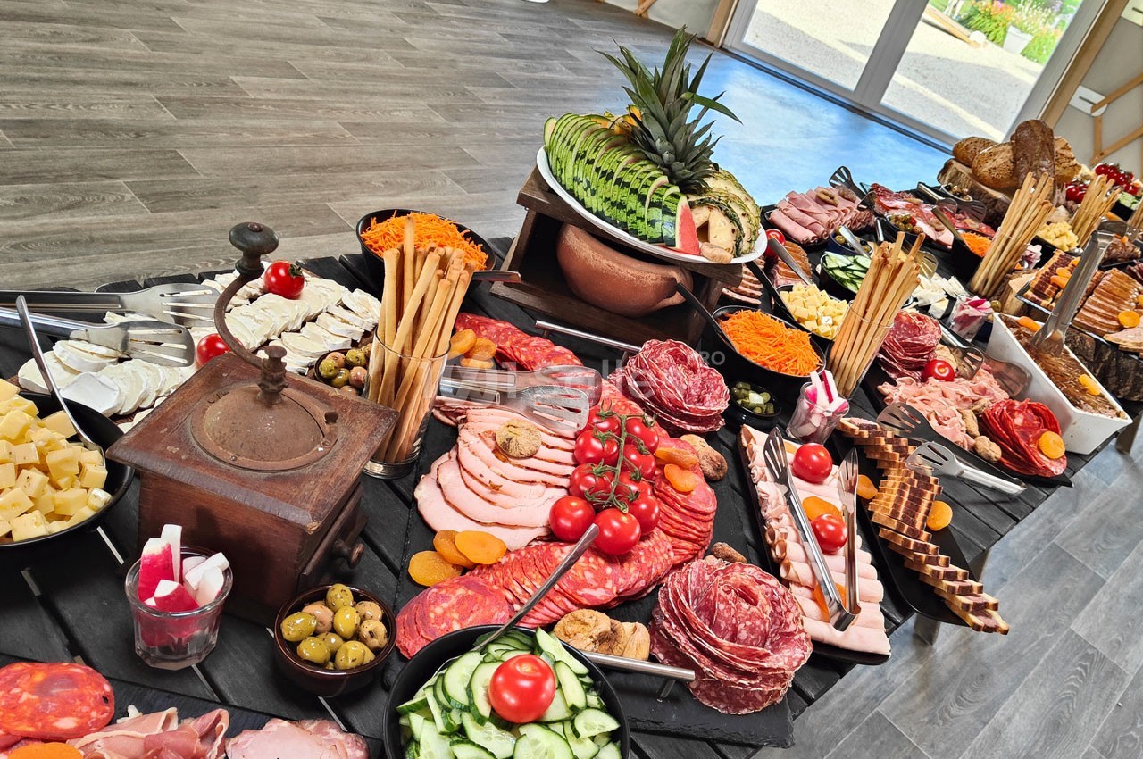 Buffet varié avec charcuteries, fromages, légumes frais, pains et fruits, présenté sur une table en bois.