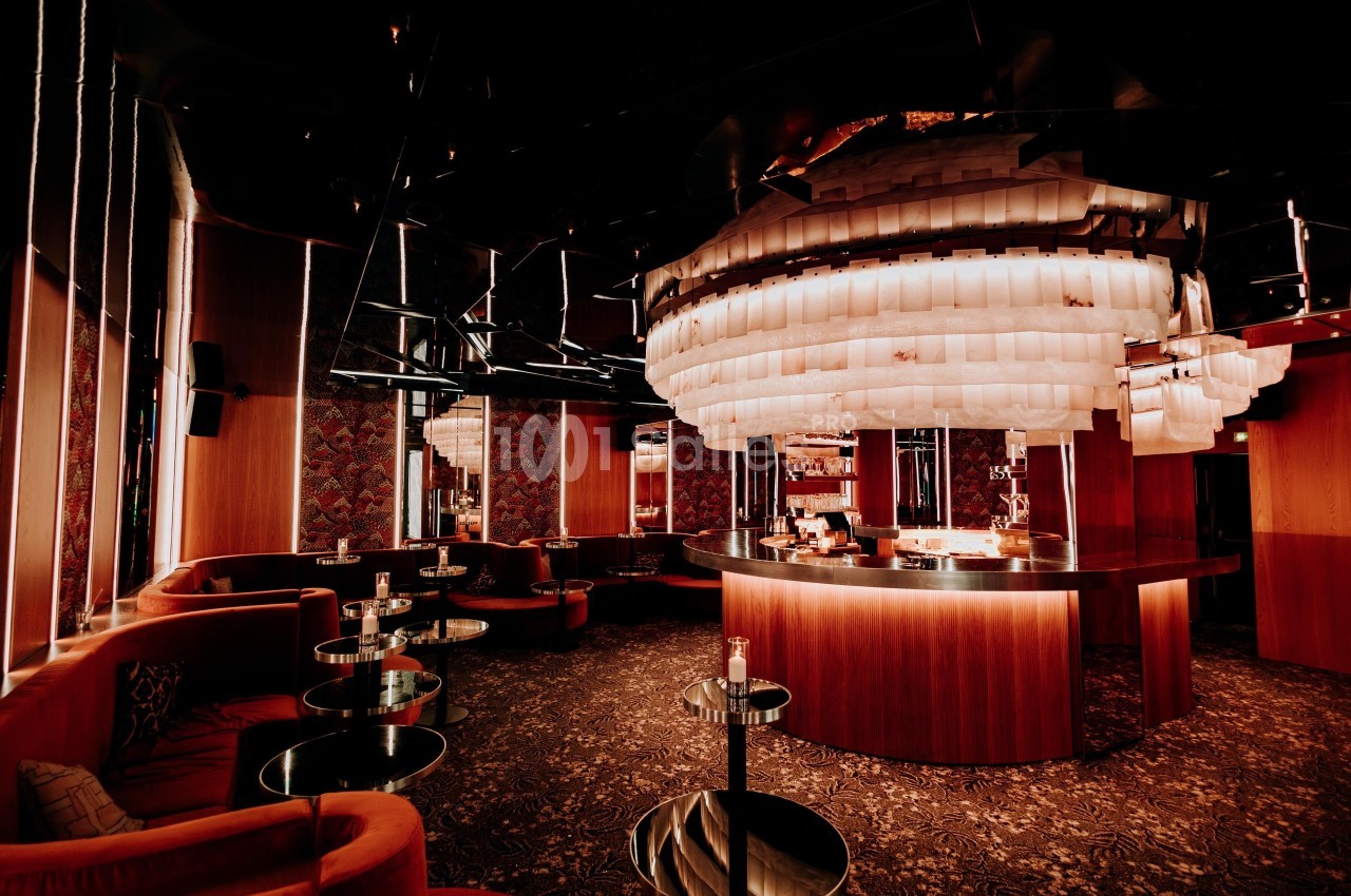 Bar élégant avec comptoir circulaire, éclairage tamisé et grand lustre moderne dans une ambiance chaleureuse.