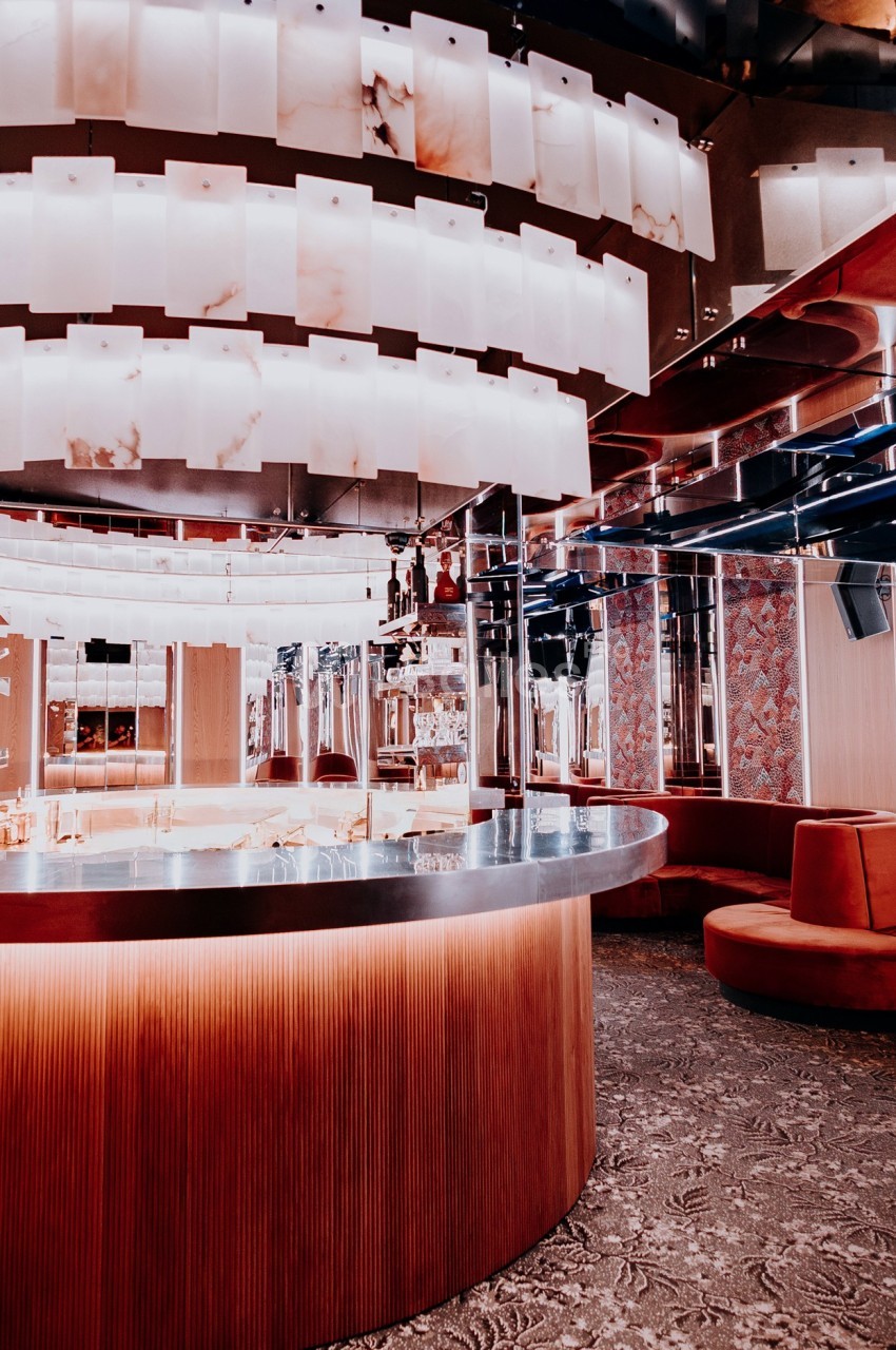Intérieur d'un bar moderne avec comptoir incurvé, éclairage suspendu et banquettes rouges.