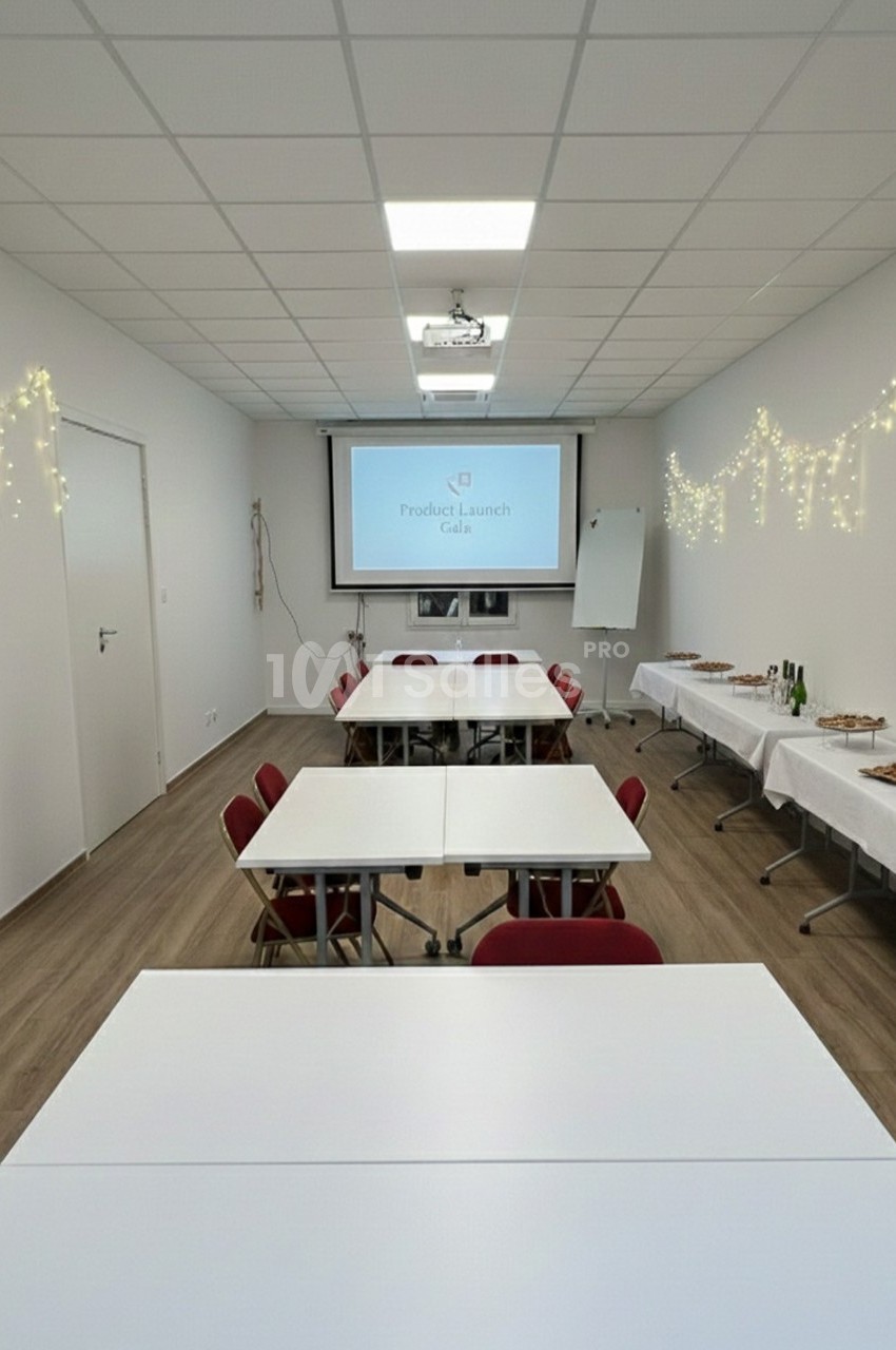 Salle de réunion décorée avec guirlandes lumineuses, tables alignées, écran de projection et buffet en arrière-plan.