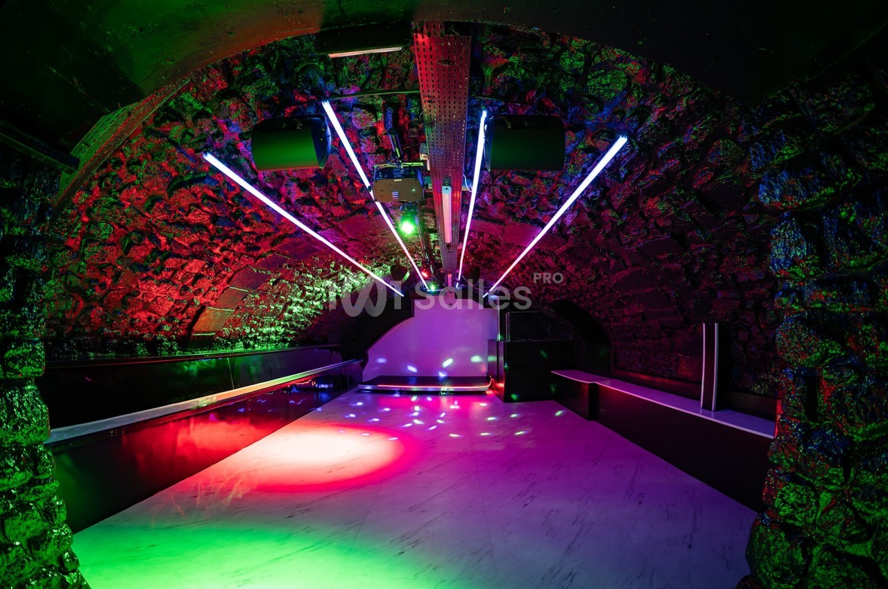 Salle voûtée en pierre avec éclairage néon coloré et sol en marbre, évoquant un espace festif ou artistique.