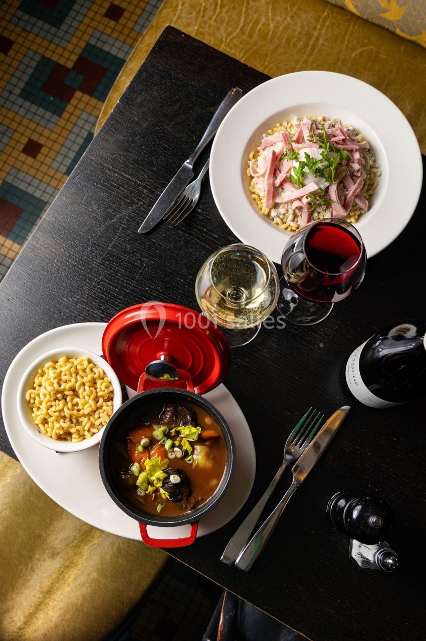 Vue de dessus d'une table avec un plat mijoté, des pâtes, une assiette de viande sur céréales et deux verres de vin.