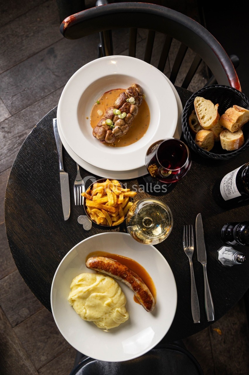 Repas composé de saucisse-purée et filet de viande avec sauce, accompagné de frites, pain, vin rouge et blanc.