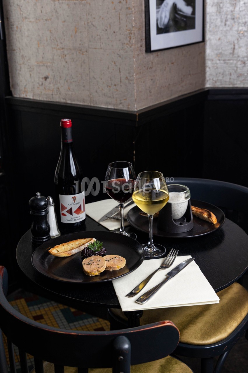 Table dressée avec deux assiettes de foie gras, verres de vin rouge et blanc, bouteille de vin et pain grillé.