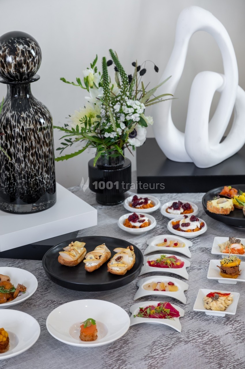 Assortiment de bouchées et amuse-bouches variés présentés sur une table avec des décorations modernes et florales.