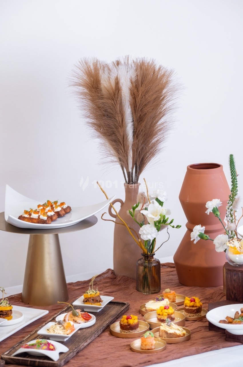 Table décorée avec des vases en céramique, des fleurs séchées et des assiettes de petits plats raffinés.