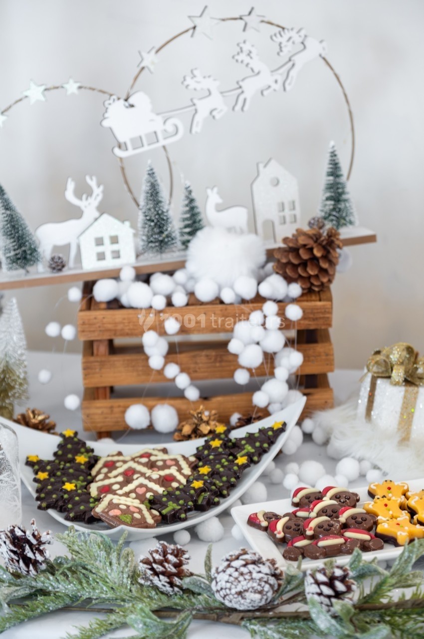 Plateau de biscuits décorés de Noël entouré de décorations festives, sapins miniatures et pommes de pin.