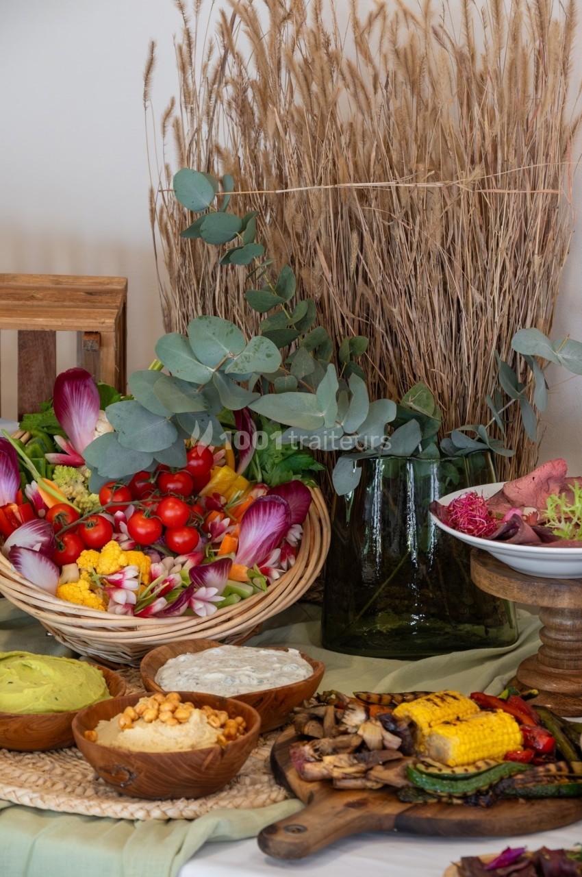 Assortiment de légumes frais, sauces et épis de maïs grillés disposés sur une table décorée de feuillages et d'épis de blé.