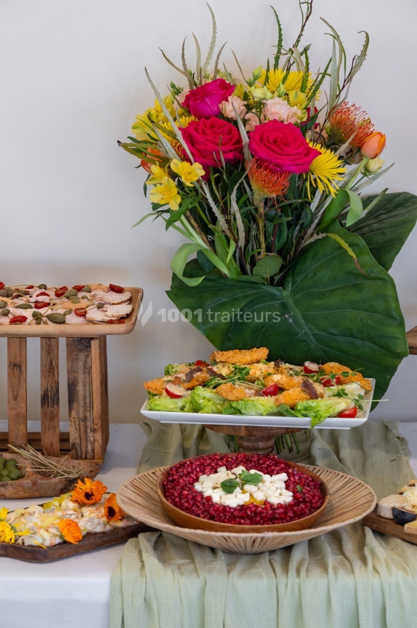 Buffet coloré avec salades, plats garnis et un bouquet de fleurs vives en arrière-plan.
