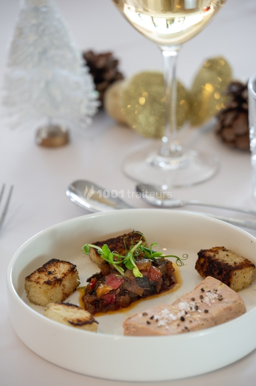 Assiette gastronomique avec foie gras, croûtons dorés et garniture, décor festif en arrière-plan.