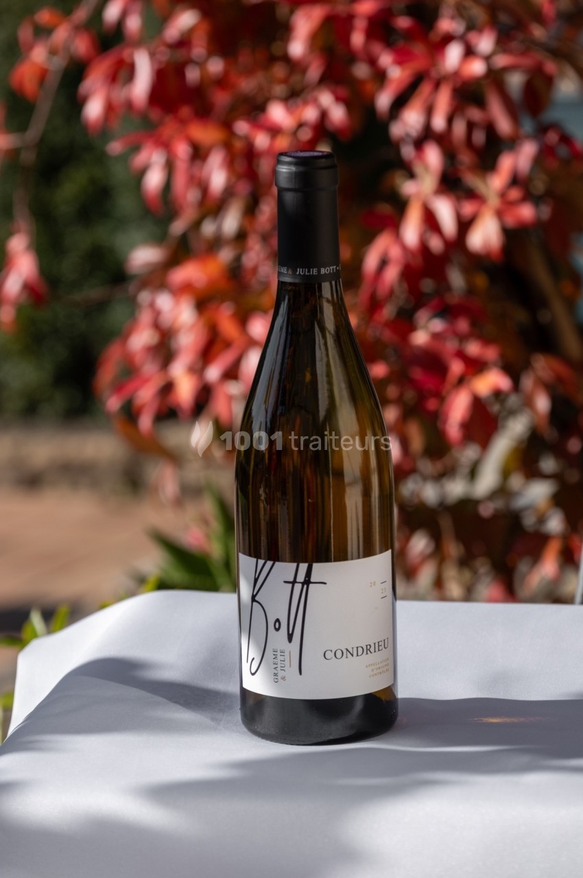 Bouteille de vin blanc Condrieu posée sur une table blanche, avec un arrière-plan de feuillage rouge et vert.