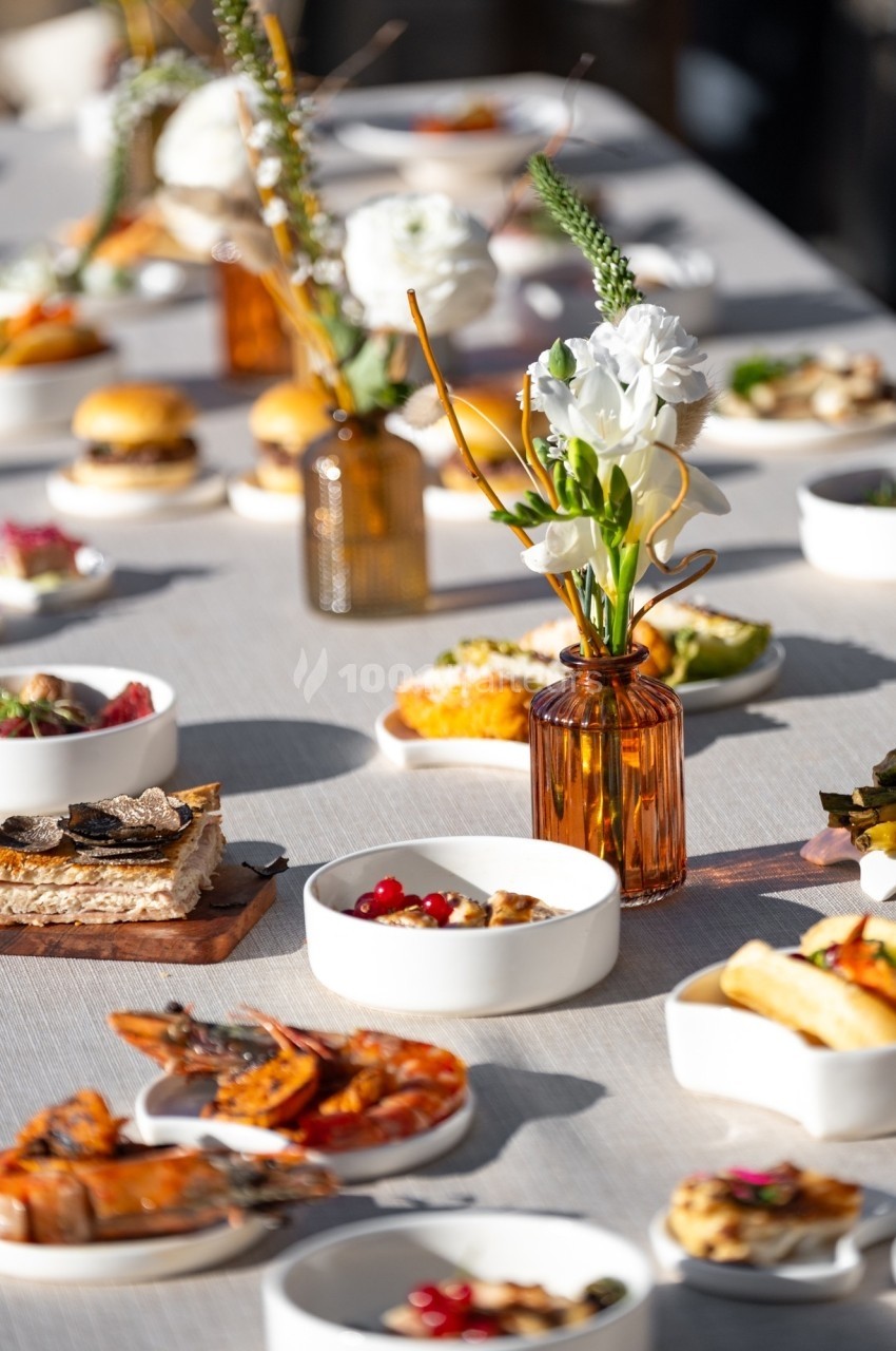 Table dressée avec des plats variés, incluant fruits de mer, tartines et desserts, décorée de fleurs blanches en vase.