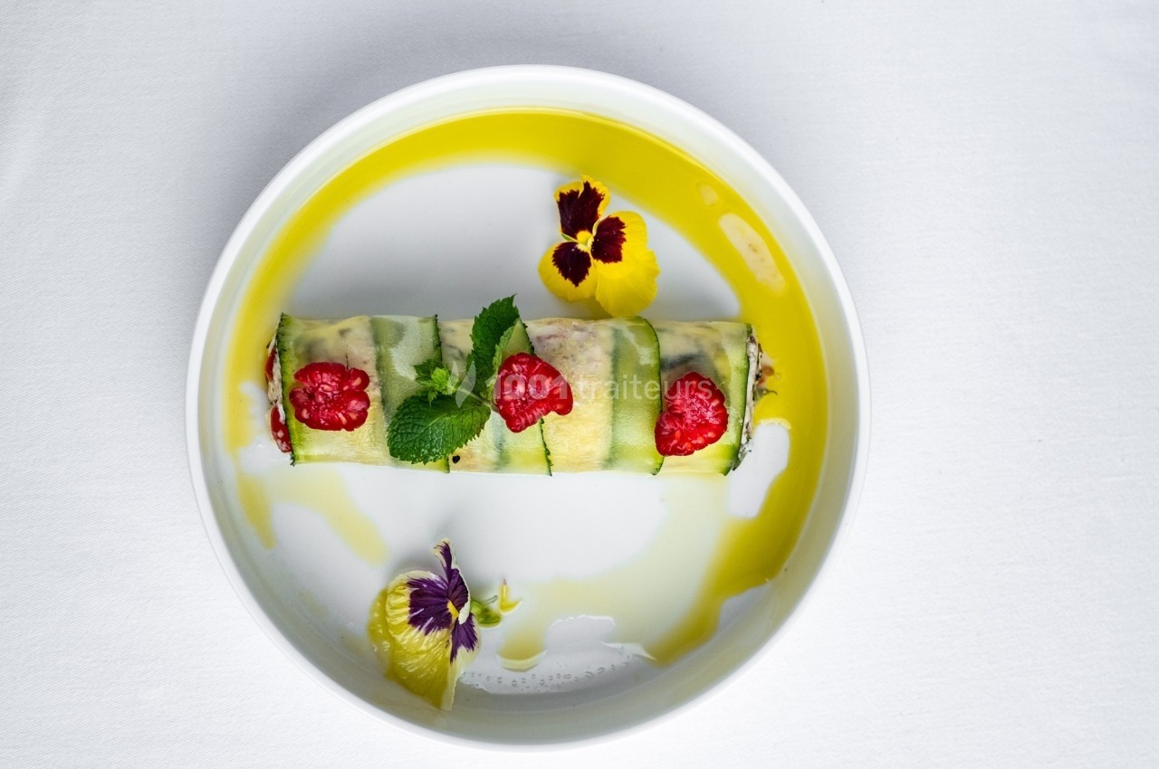 Rouleau de légumes garnis de framboises, décoré de fleurs comestibles et d'une sauce jaune sur une assiette blanche.