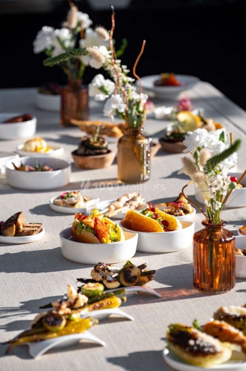 Table dressée avec divers plats raffinés et colorés, accompagnés de vases contenant des fleurs décoratives.