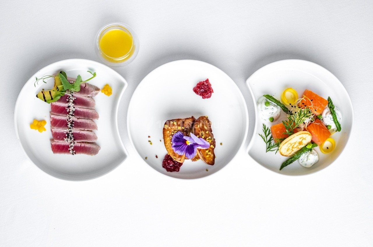 Trois assiettes contenant des plats raffinés : thon, foie gras et saumon, accompagnés de garnitures et sauces.