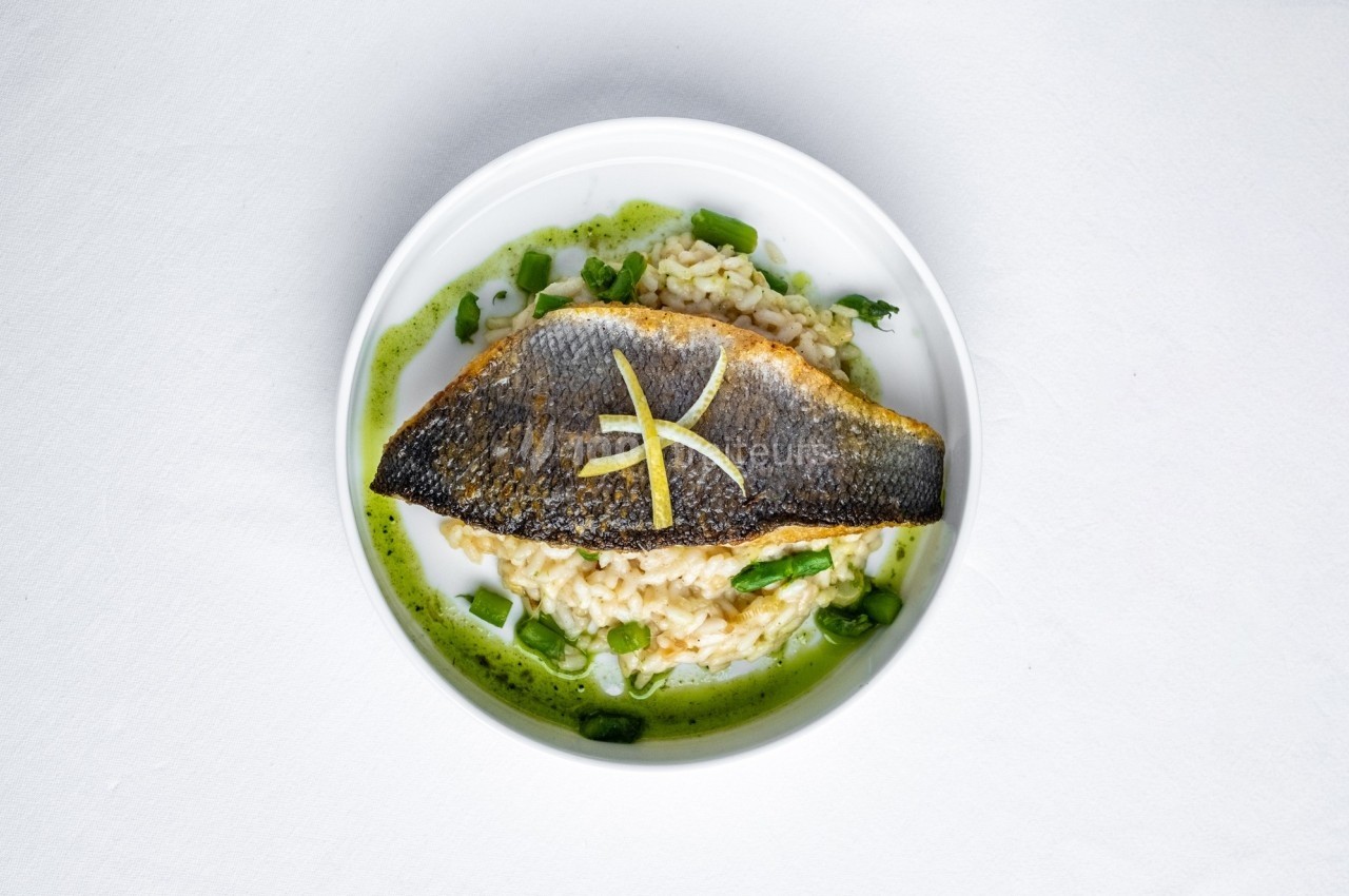 Filet de poisson grillé sur risotto crémeux, accompagné d'asperges et d'une sauce verte.