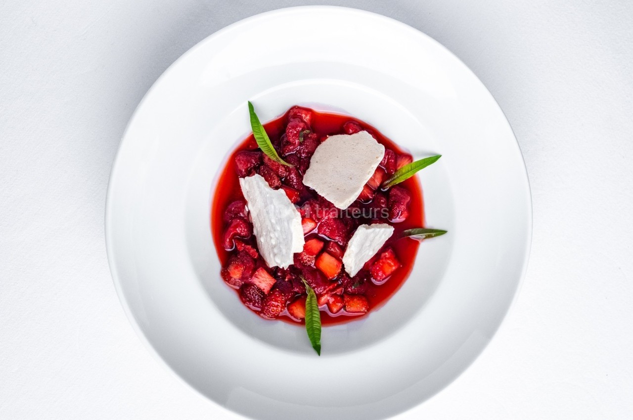 Dessert composé de fruits rouges, morceaux de meringue et feuilles décoratives, présenté dans une assiette blanche.