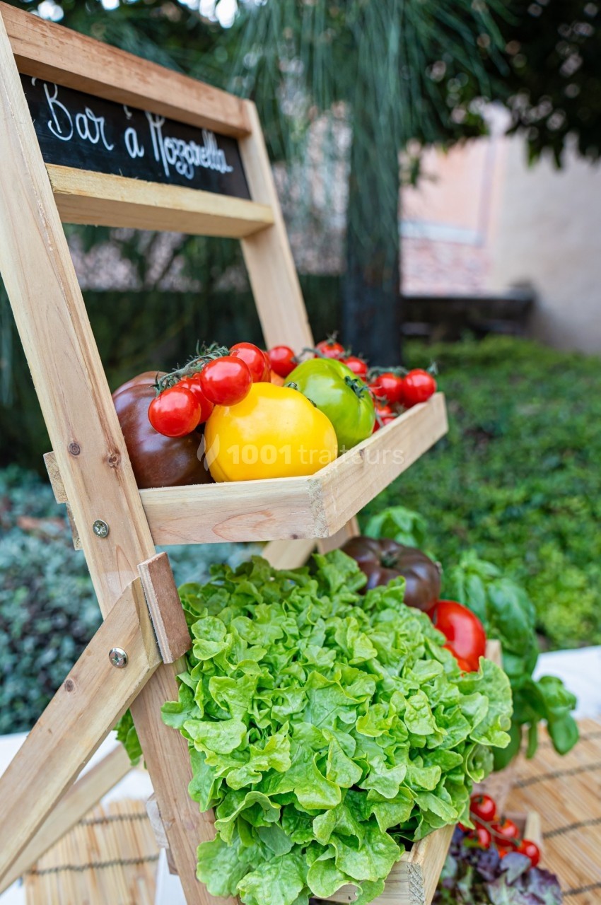 Présentoir en bois avec des légumes frais, dont tomates, poivrons et laitue, disposé en extérieur près de végétation.