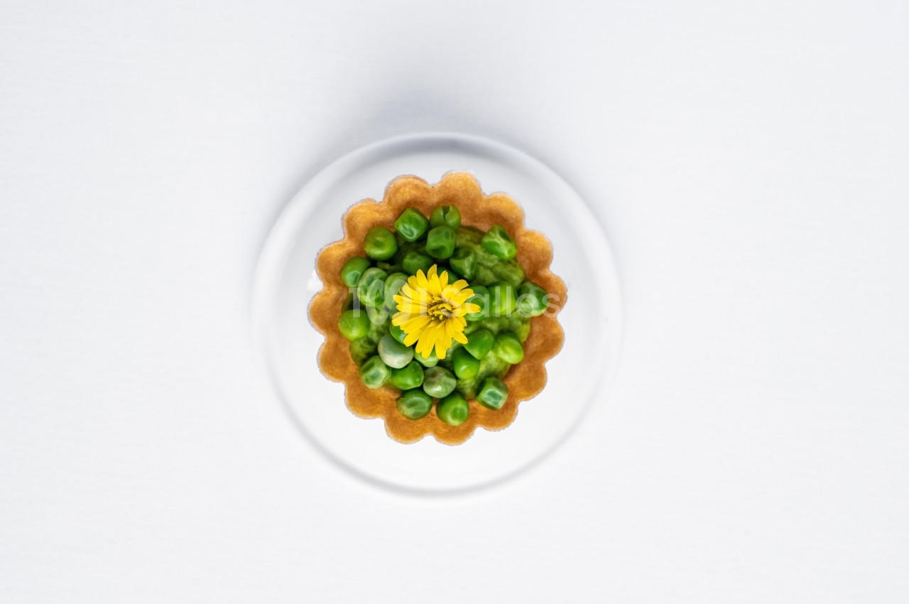 Tartelette garnie de petits pois verts et décorée d'une fleur jaune, présentée sur une assiette blanche.