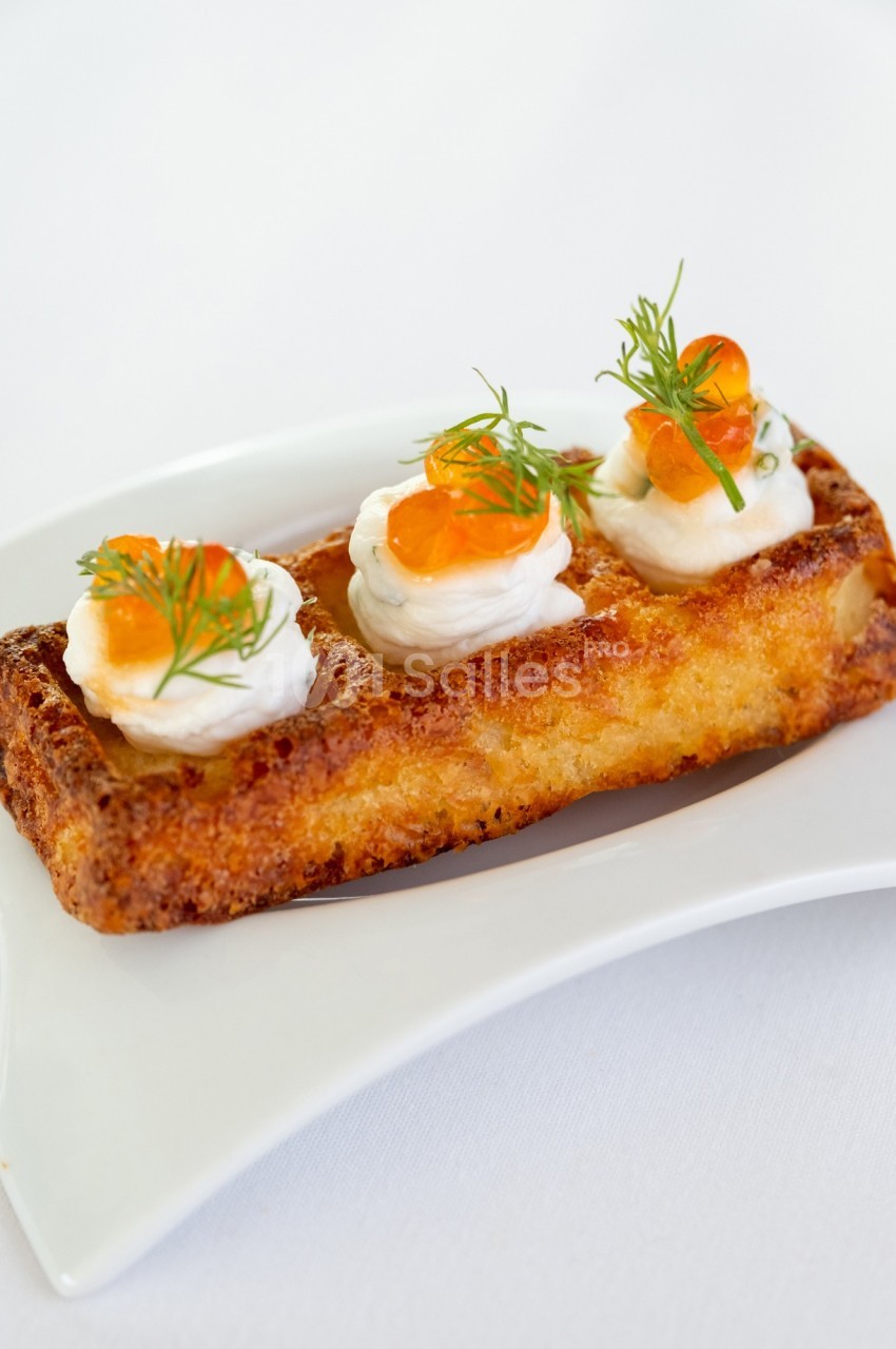 Gaufre dorée garnie de crème, œufs de poisson et brins d'aneth, servie sur une assiette blanche.