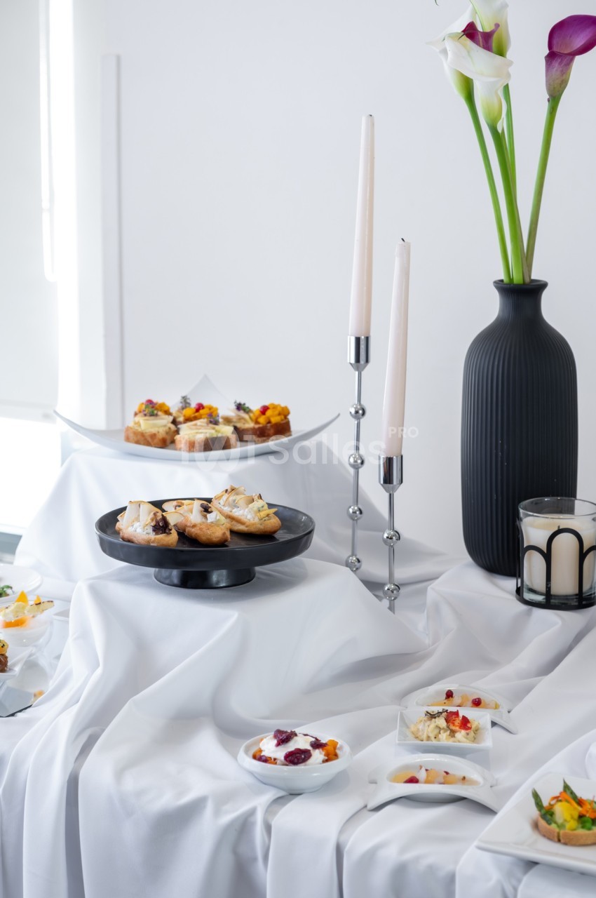 Table dressée avec des amuse-bouches variés, des bougies blanches et un vase noir contenant des callas.