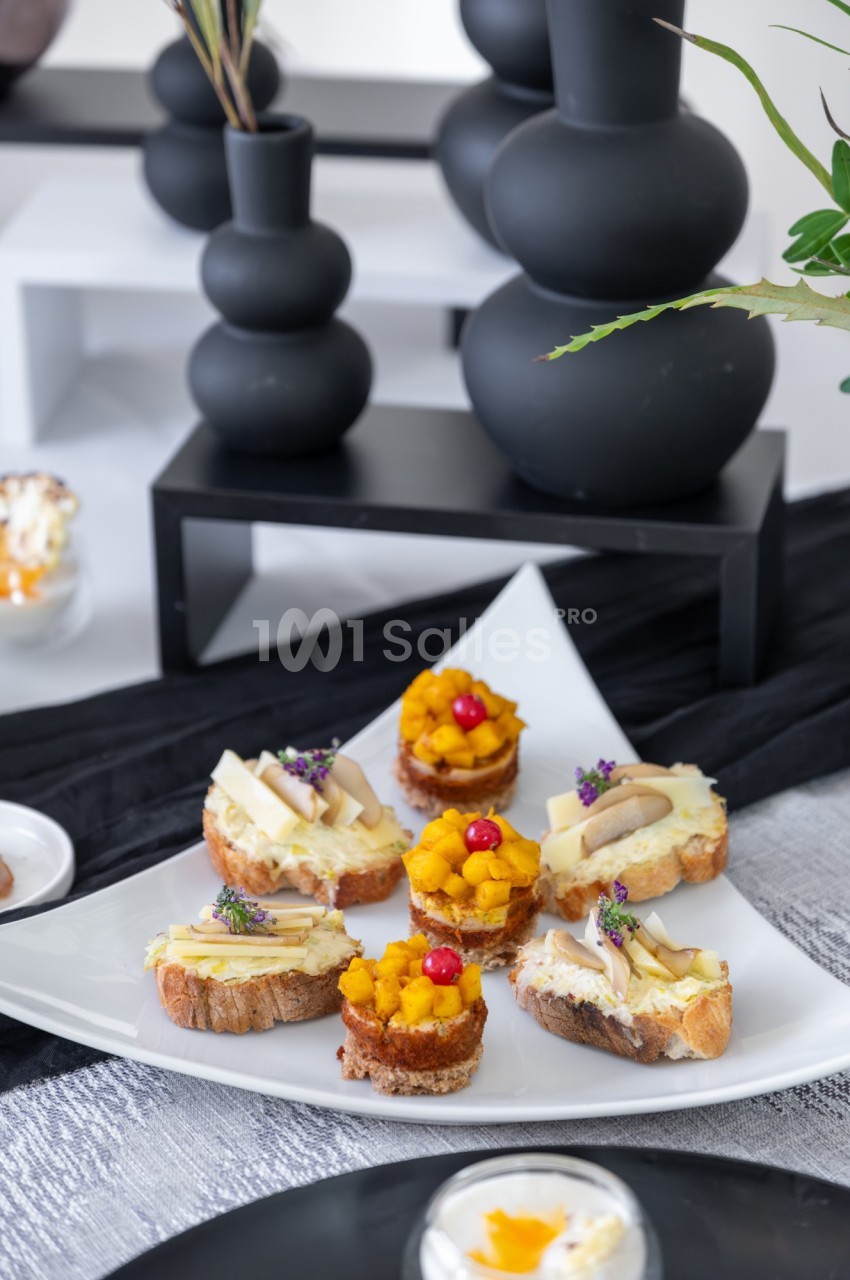 Assortiment de toasts garnis de fromage, purée de courge et baies rouges, présentés sur une assiette blanche.
